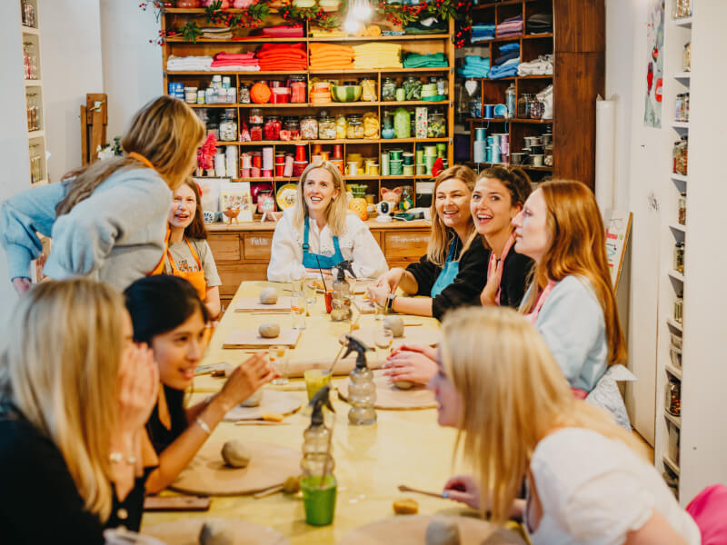 A group of people sat around a table smiling at a pottery class.